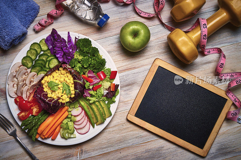 素食主题。Table top view of spring salad on rustic wooden table with dumbbells', tape measure and towel